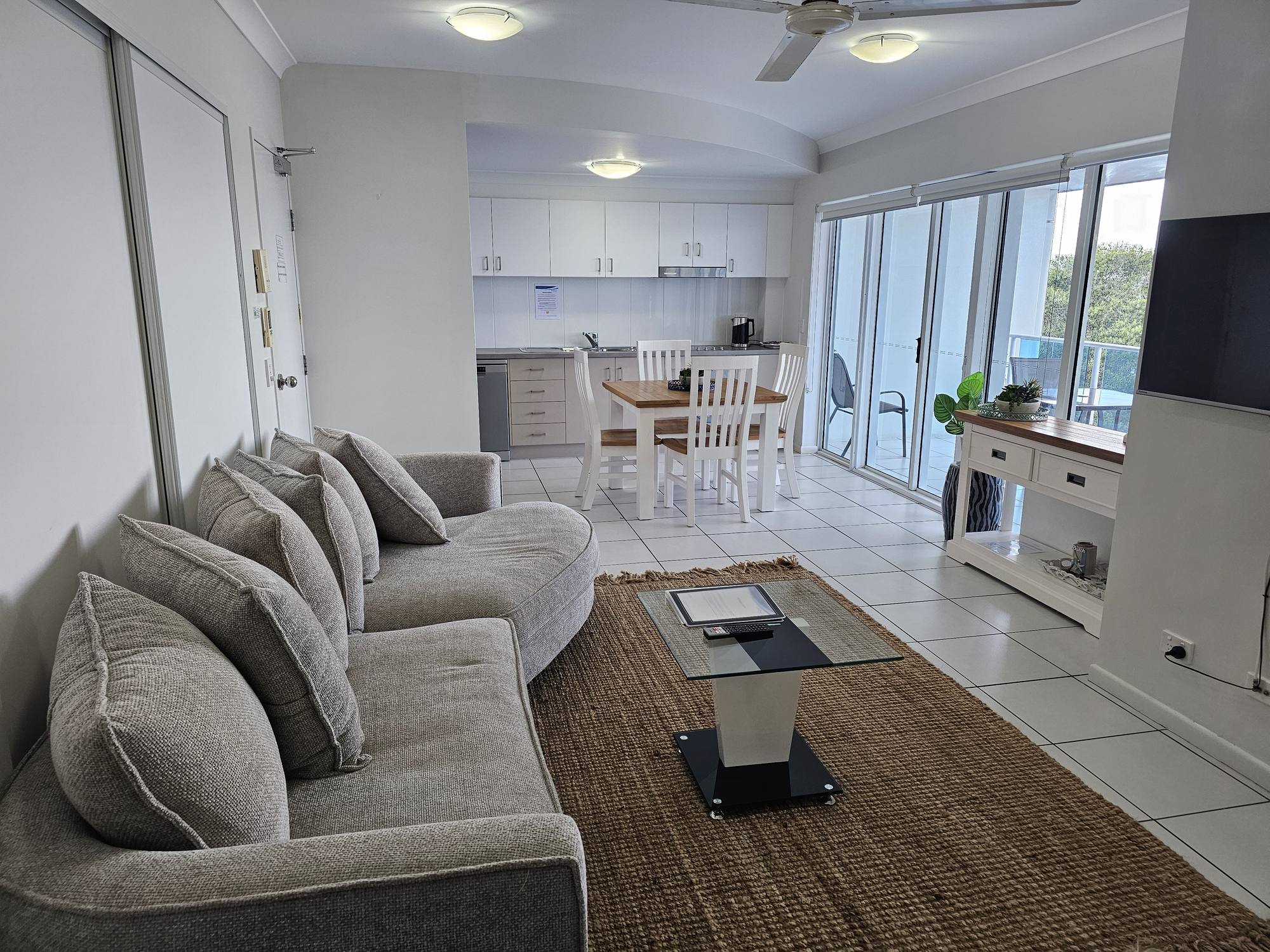 Bargara Vista apartment 502 lounge with grey sofa, white kitchen and dining table, balcony doors open to the view