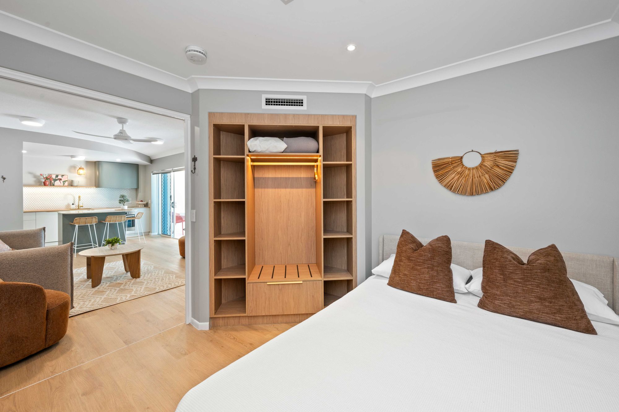 Queen bedroom in Koola Palms 101 with rust cushions, timber built-in wardrobe and view through to the living area