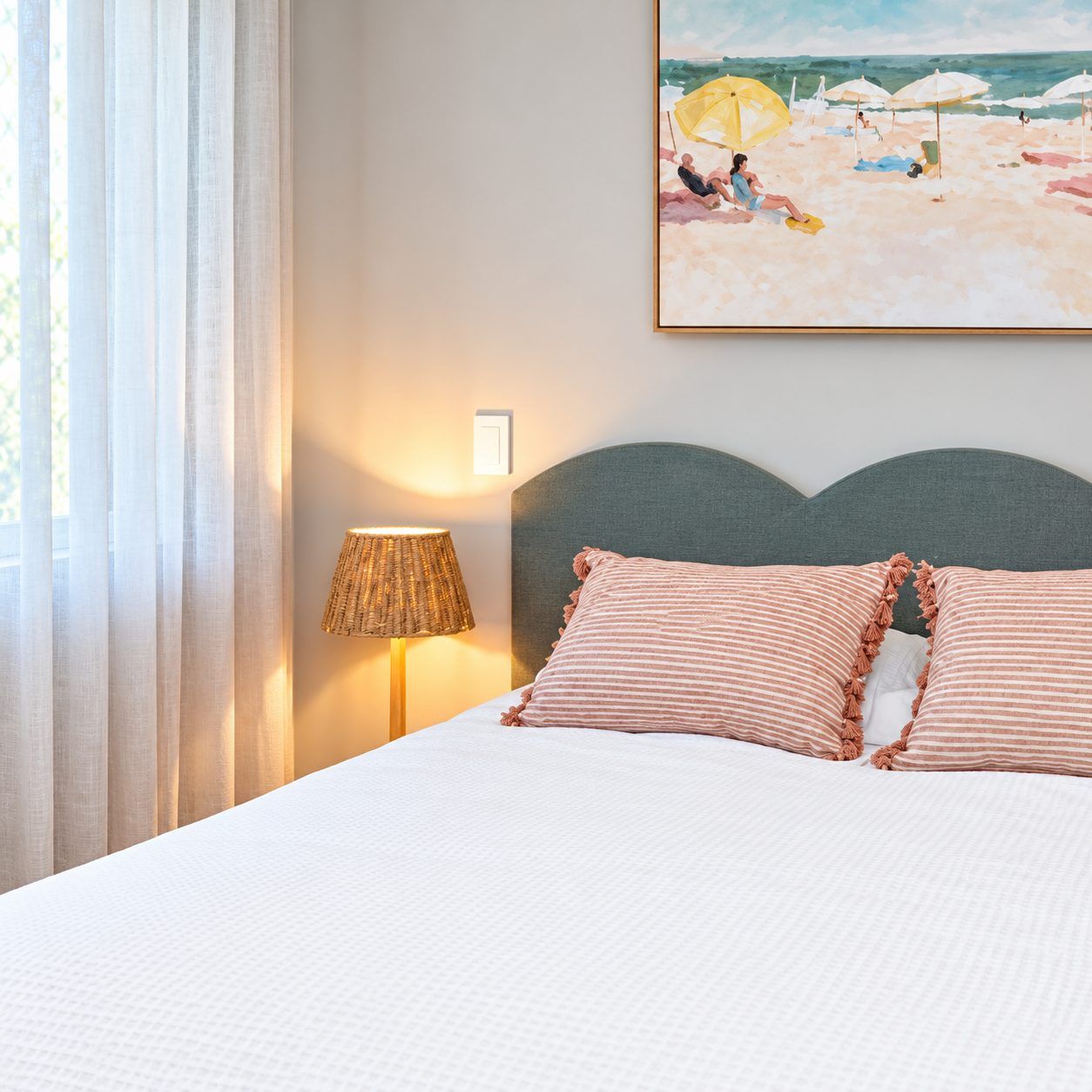 Queen bed in Koola Palms 101 with a grey scalloped headboard, striped cushions, rattan lamp and beach artwork